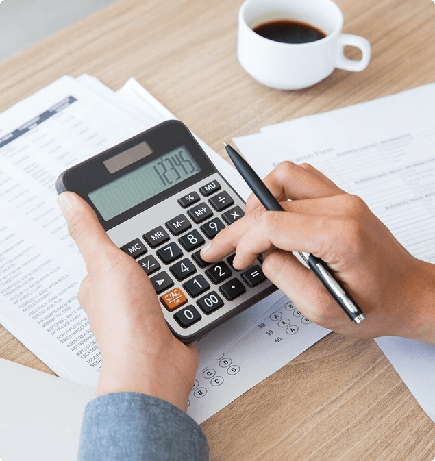 Accountant using a calculator over printed sales reports beside a cup of coffee