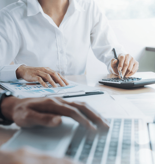Payroll professional checking her phone at a desk with reports on the monitor